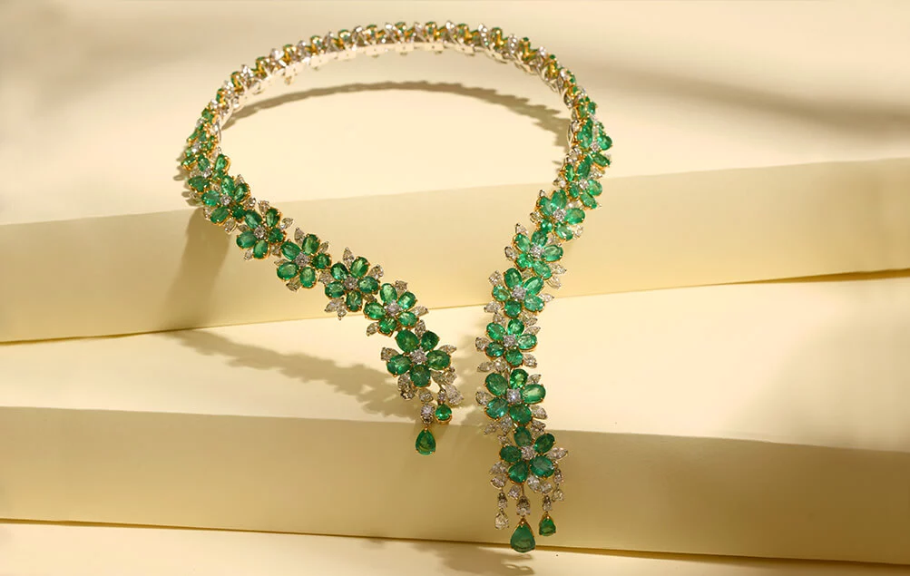 A close-up photo of a diamond and emerald necklace resting on a stack of velvet boxes.